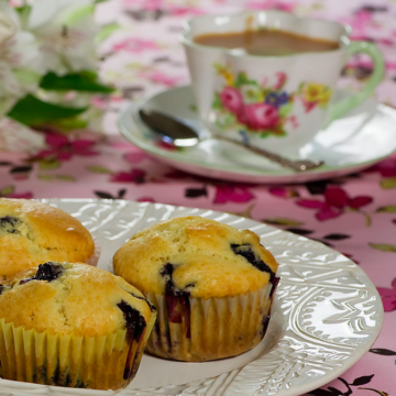 Maple syrup blueberry muffins on a white plate with a cup of tea.