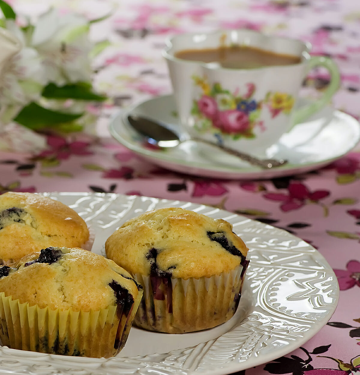 Maple blueberry muffins on a plate with a cup of tea.