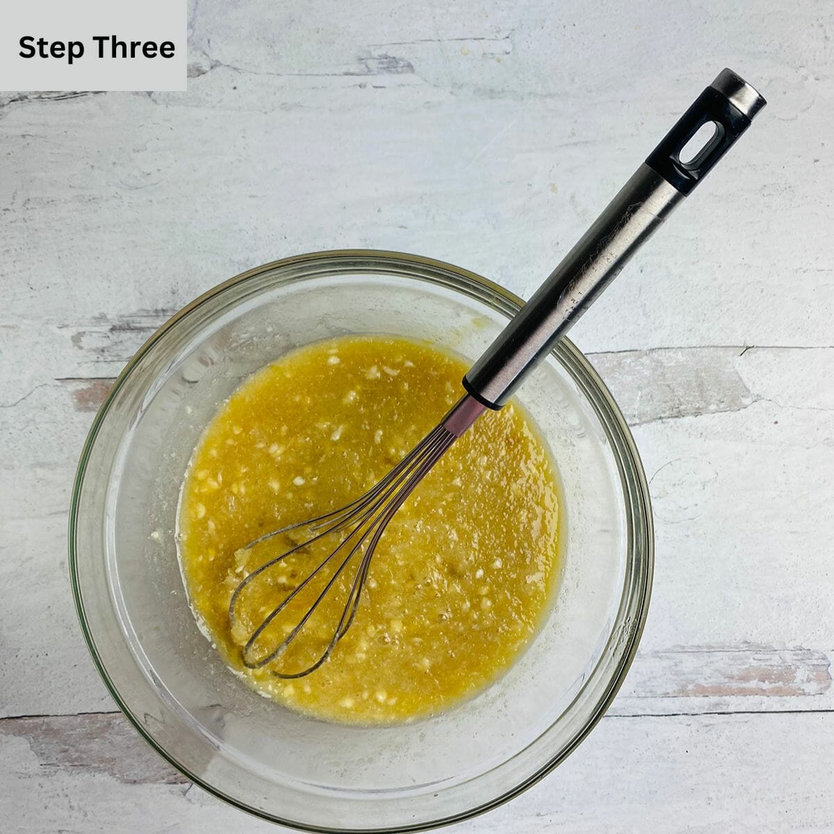 Maple syrup and egg mixture in a mixing bowl with a whisk.