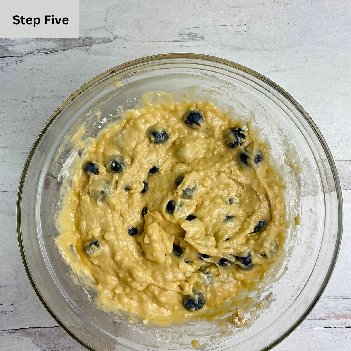 Maple blueberry muffin batter in a mixing bowl with a spatula.