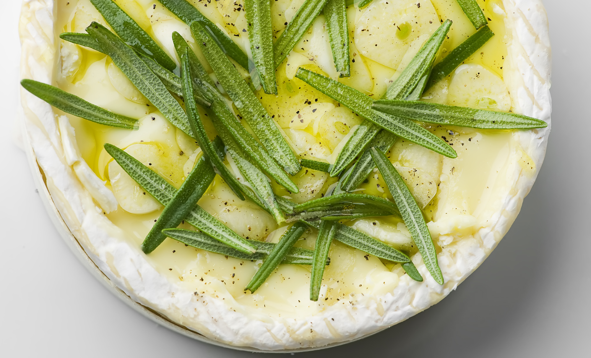 Wheel of Camembert pasta with rosemary leaves and sliced garlic.