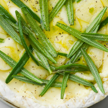 Wheel of camembert cheese with rosemary and sliced garlic.