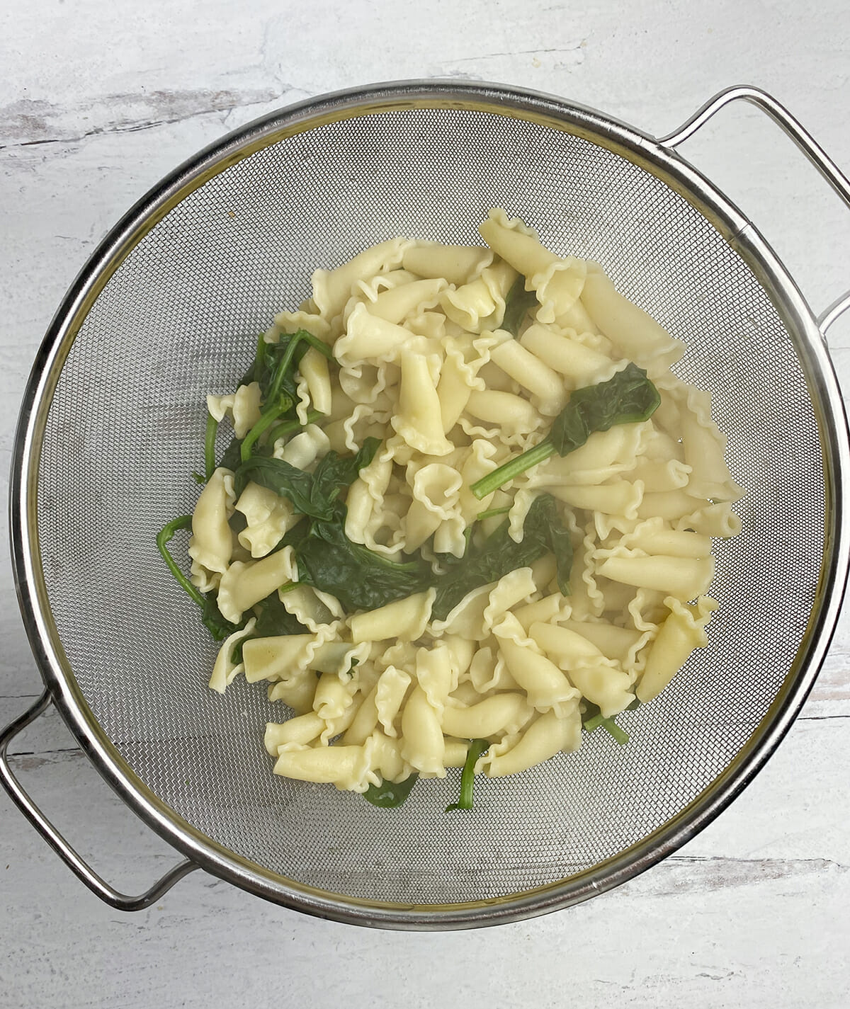 Pasta and spinach draining in a strainer.