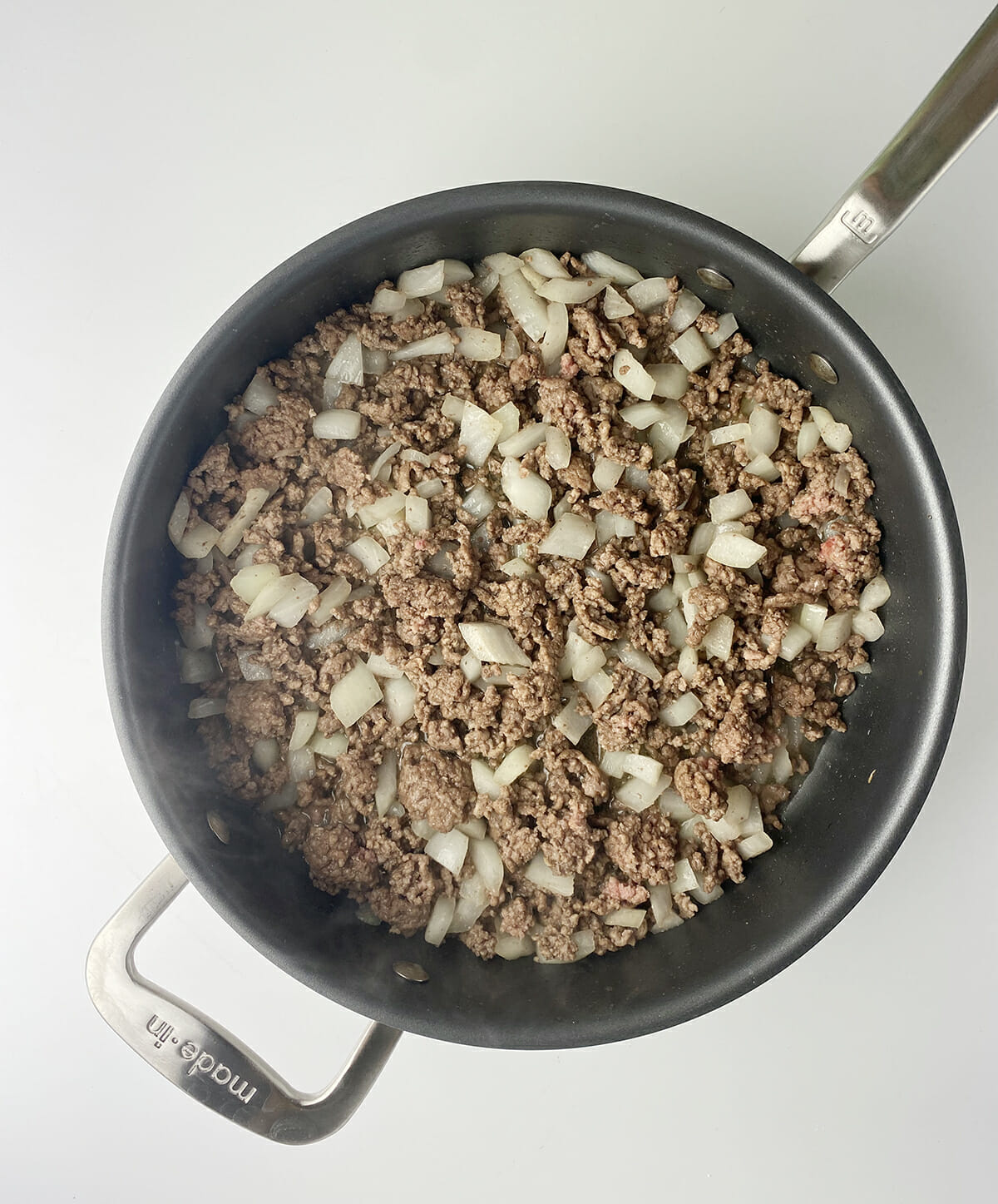 Ground beef and onion in a frying pan.