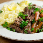 Shredded pot roast on a plate with mashed potatoes.