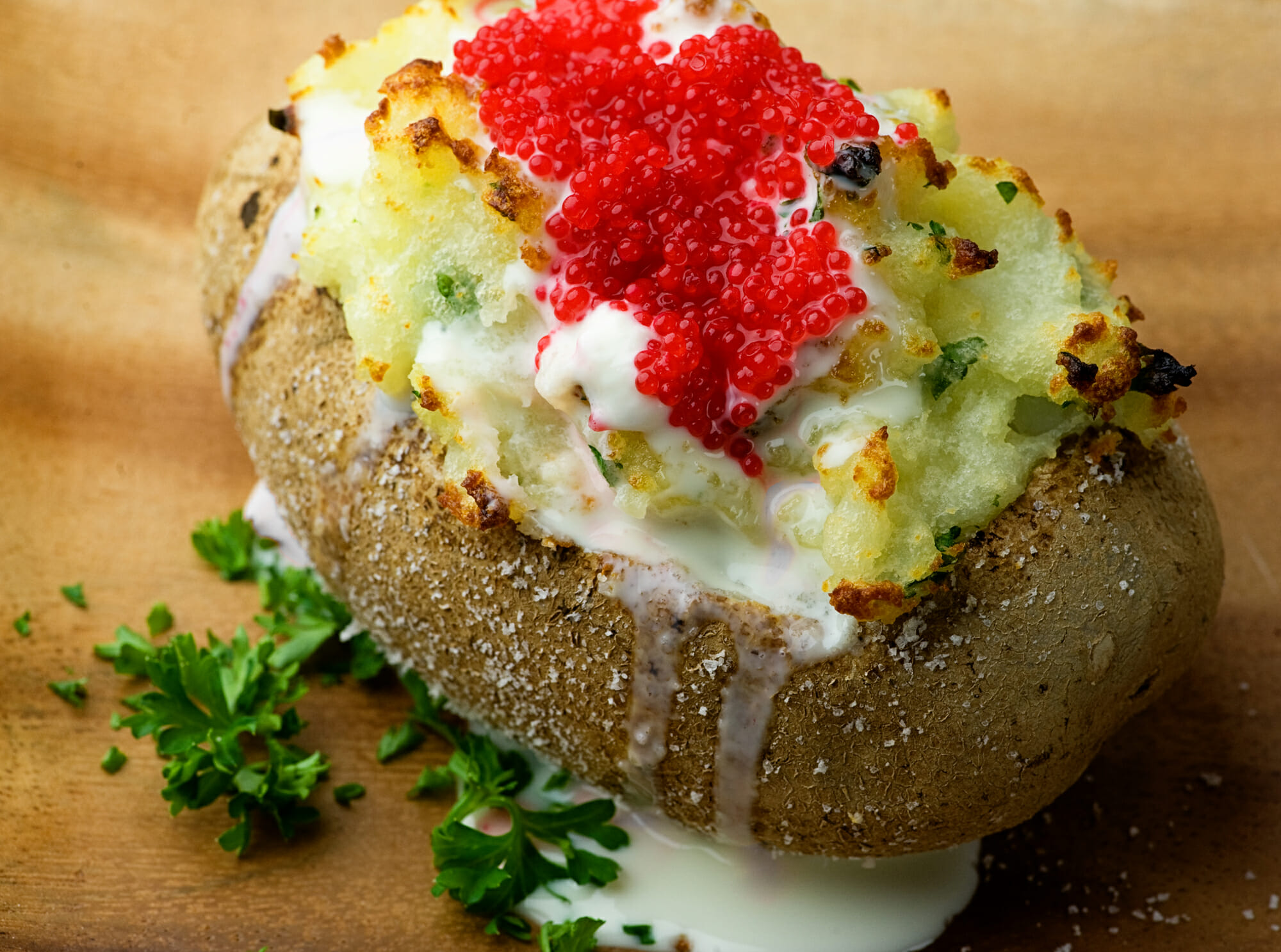 Baked potato with sour cream and caviar topping on a wooden plate.