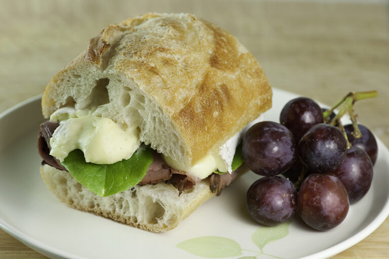 Roast Beef and Brie Sandwich with grapes on a plate.
