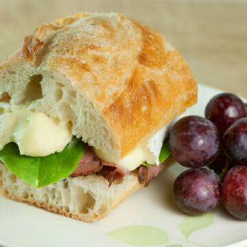 Roast beef and brie sandwich on a plate with grapes.
