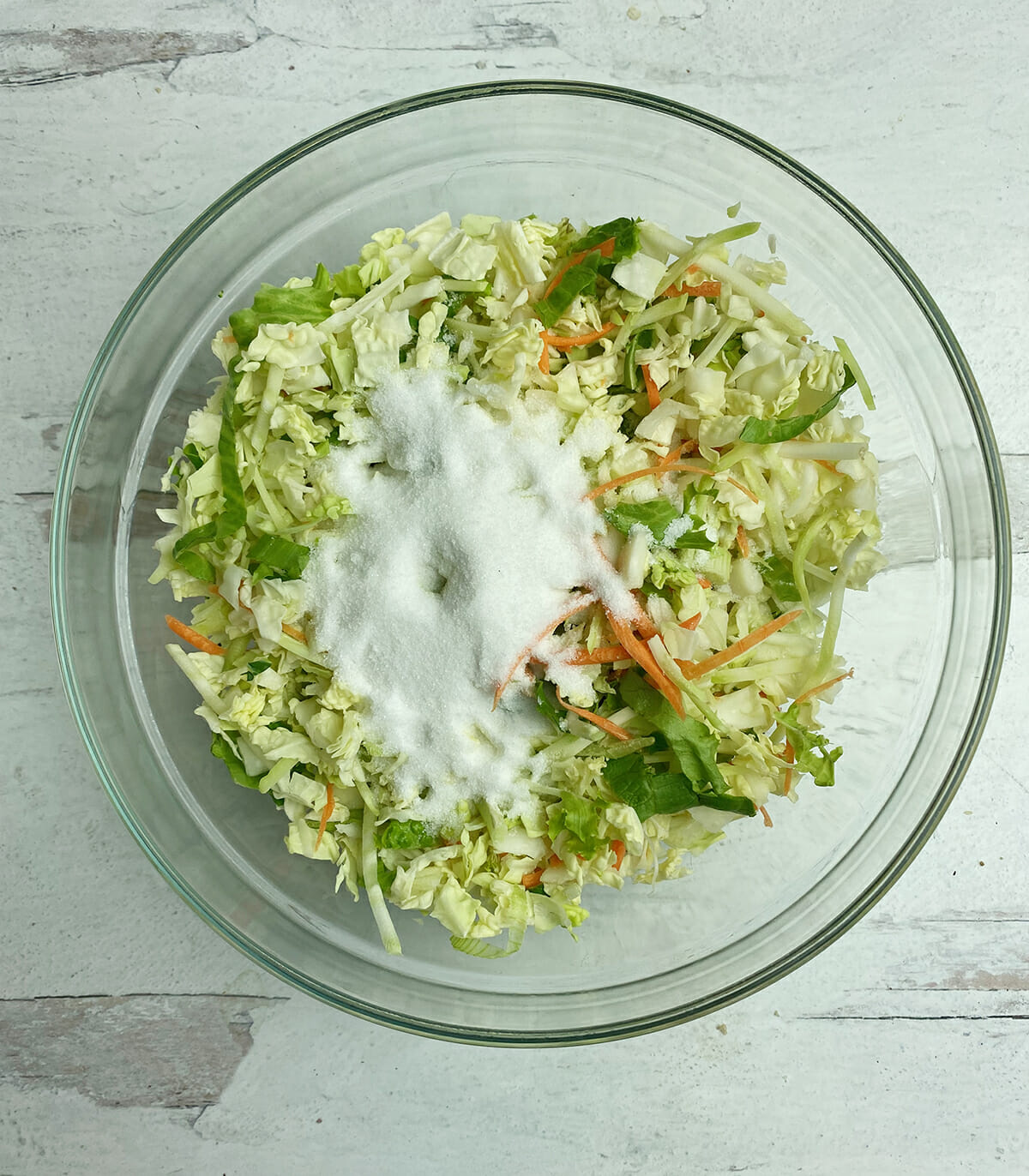Coleslaw mixture with sugar and salt in a bowl.