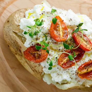 Baked Potato with Ricotta and tomatoes on a wooden board.