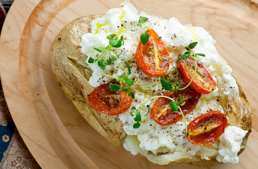 Baked Potato with Ricotta and tomatoes on a wooden board.
