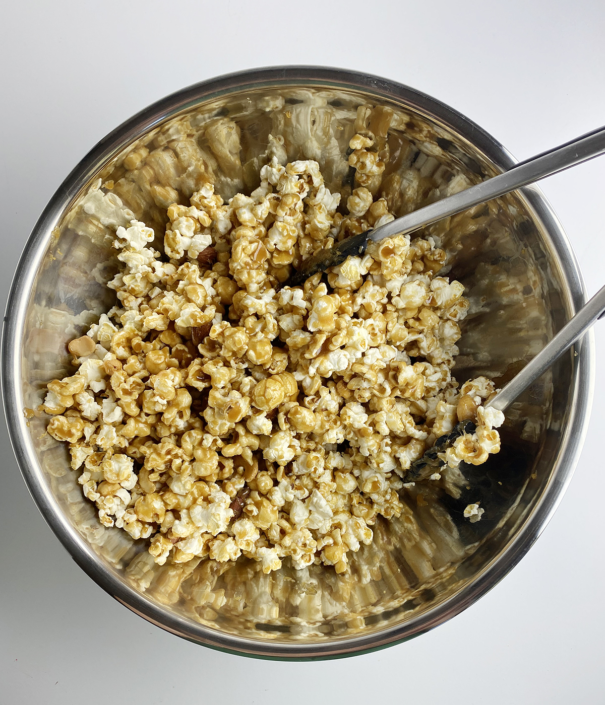 Mixing caramel coating into popcorn with tongs.