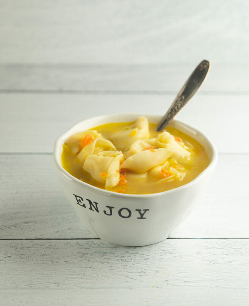 Chicken tortellini soup in a bowl with a spoon.