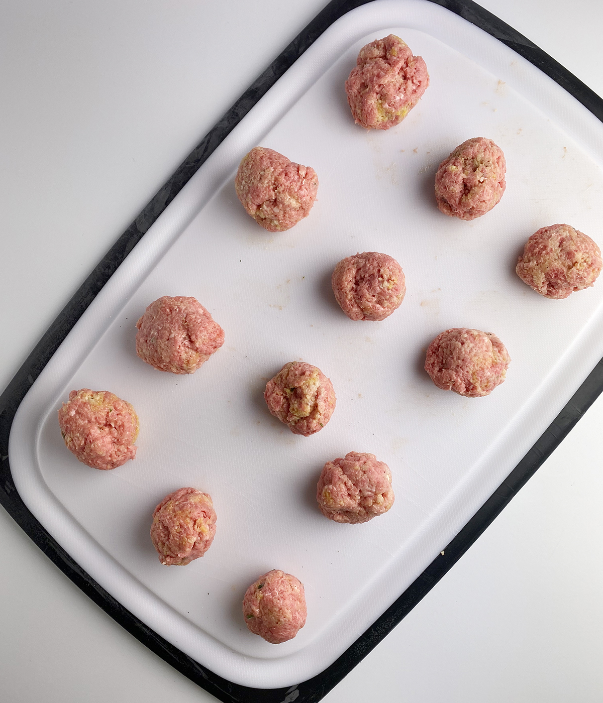Rolled meatballs on a cutting board waiting to be cooked.