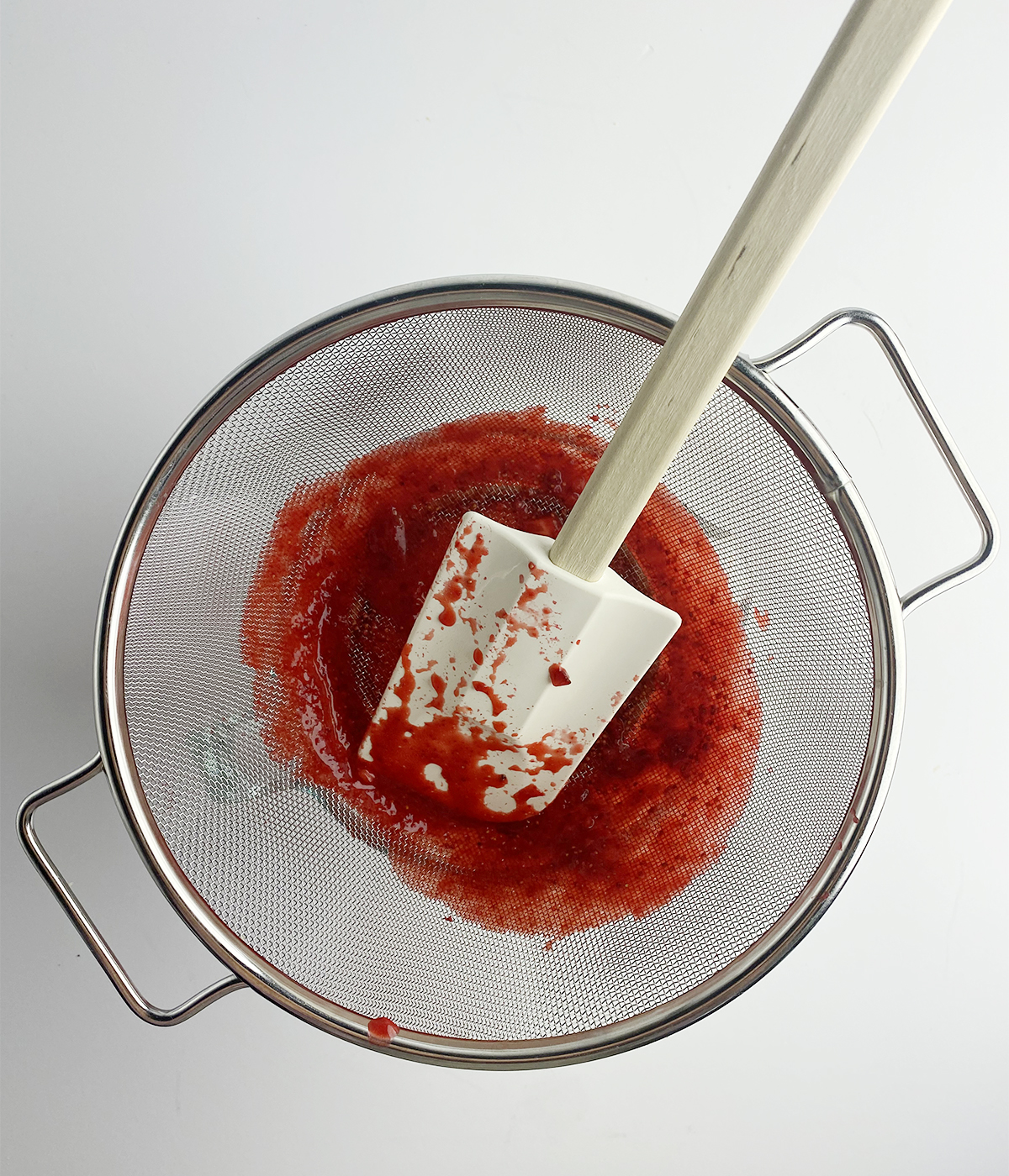 Straining pureed strawberries through a fine mesh strainer.
