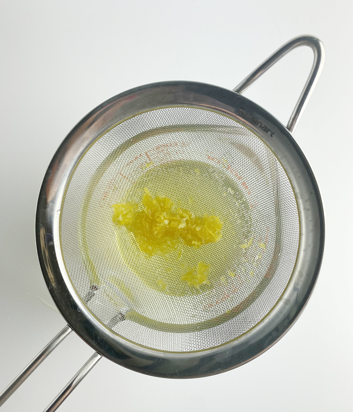 Straining the lemon sugar syrup into a measuring cup.