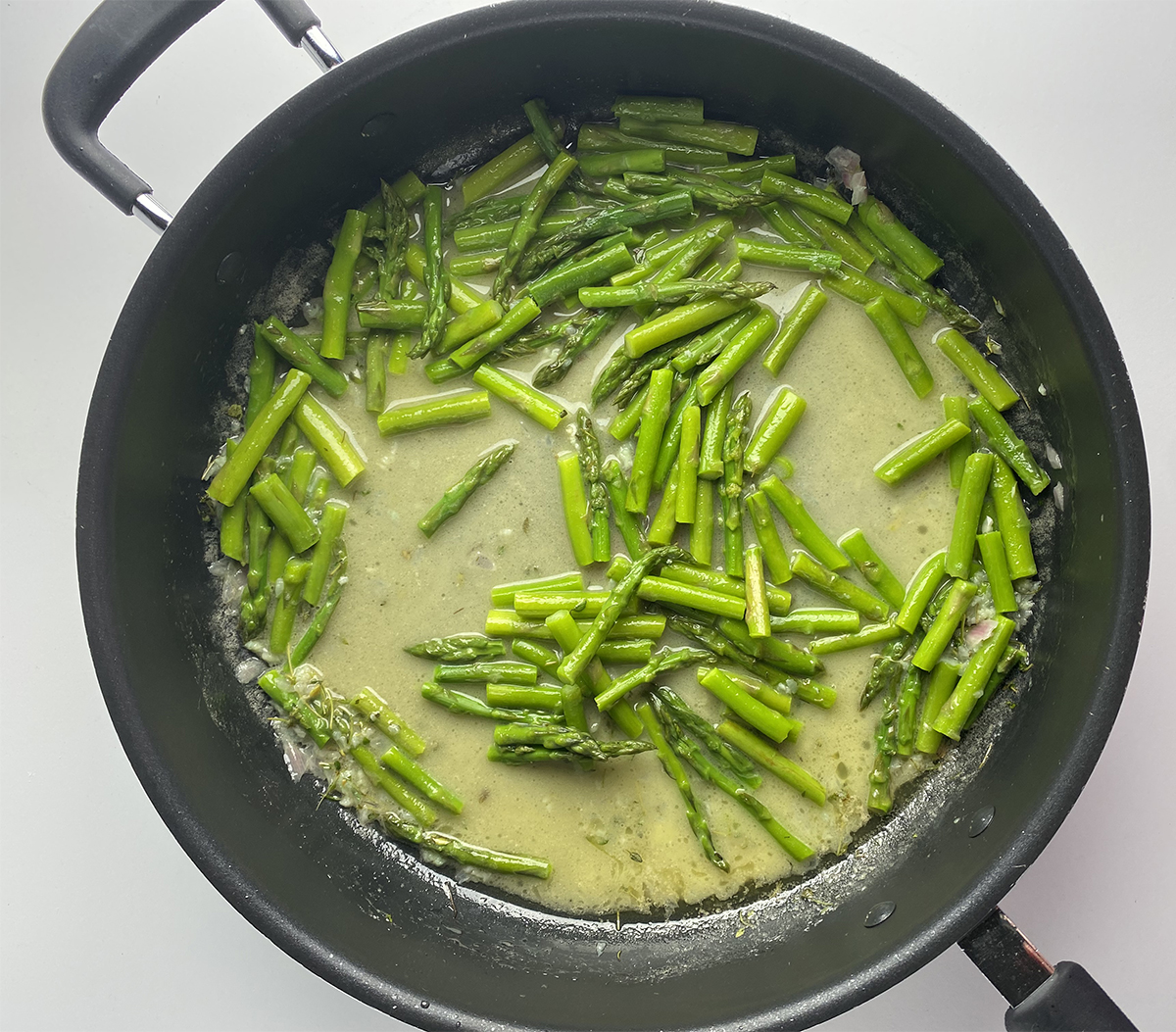 Asparagus in butter sauce in a skillet.