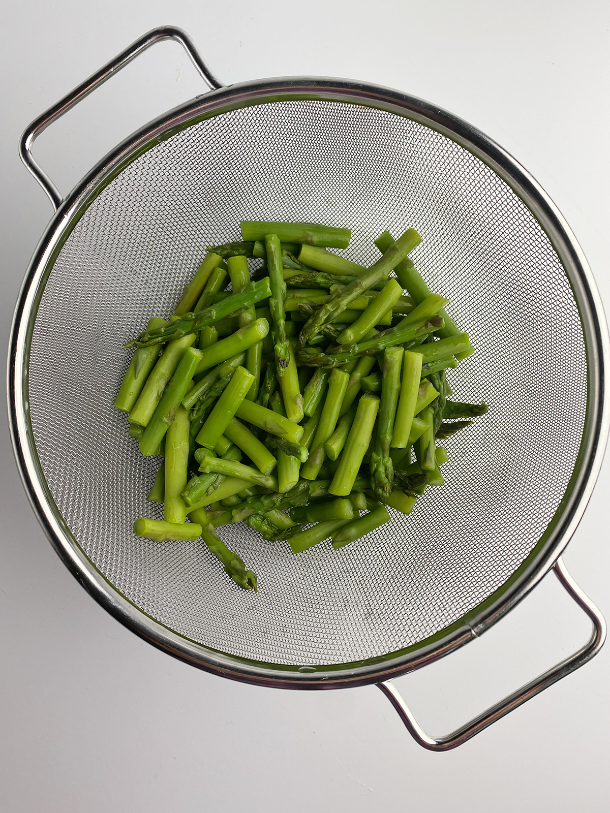 Cooked and drained asparagus in a strainer.