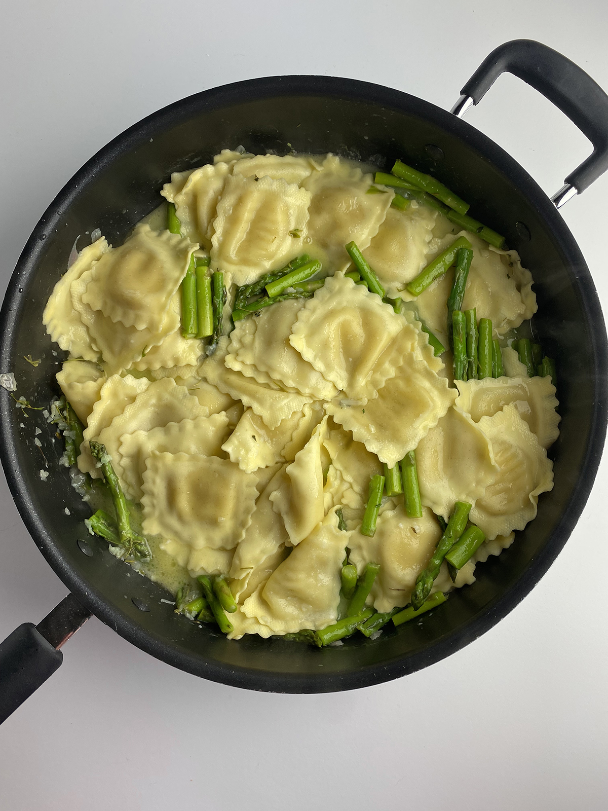 Ravioli and asparagus in pan with sauce.