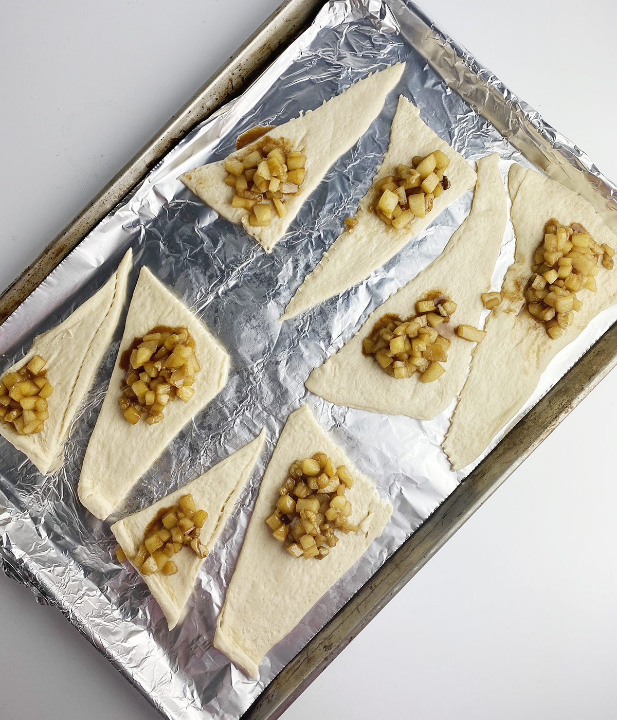 mini apple pie filling on dough resting on baking pan.