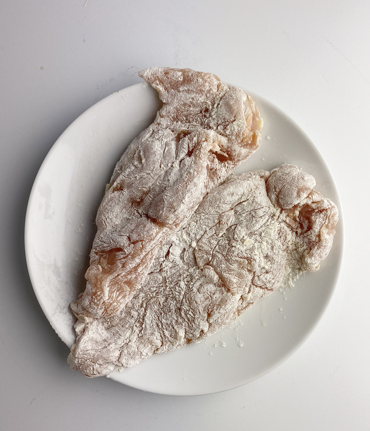 Flour dredged chicken breasts on a plate.