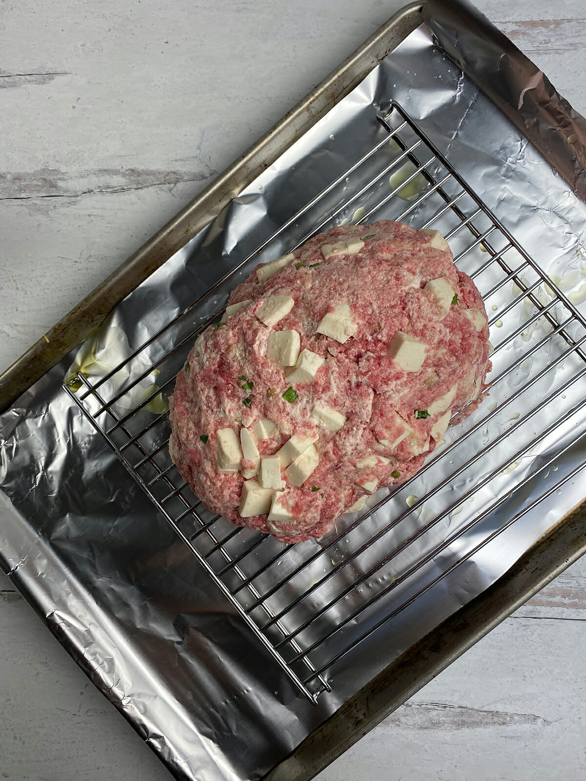 Uncooked ricotta meatloaf on a cooking sheet with a rack.