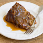 Slice of apple cake covered with caramel sauce on a plate with a fork.