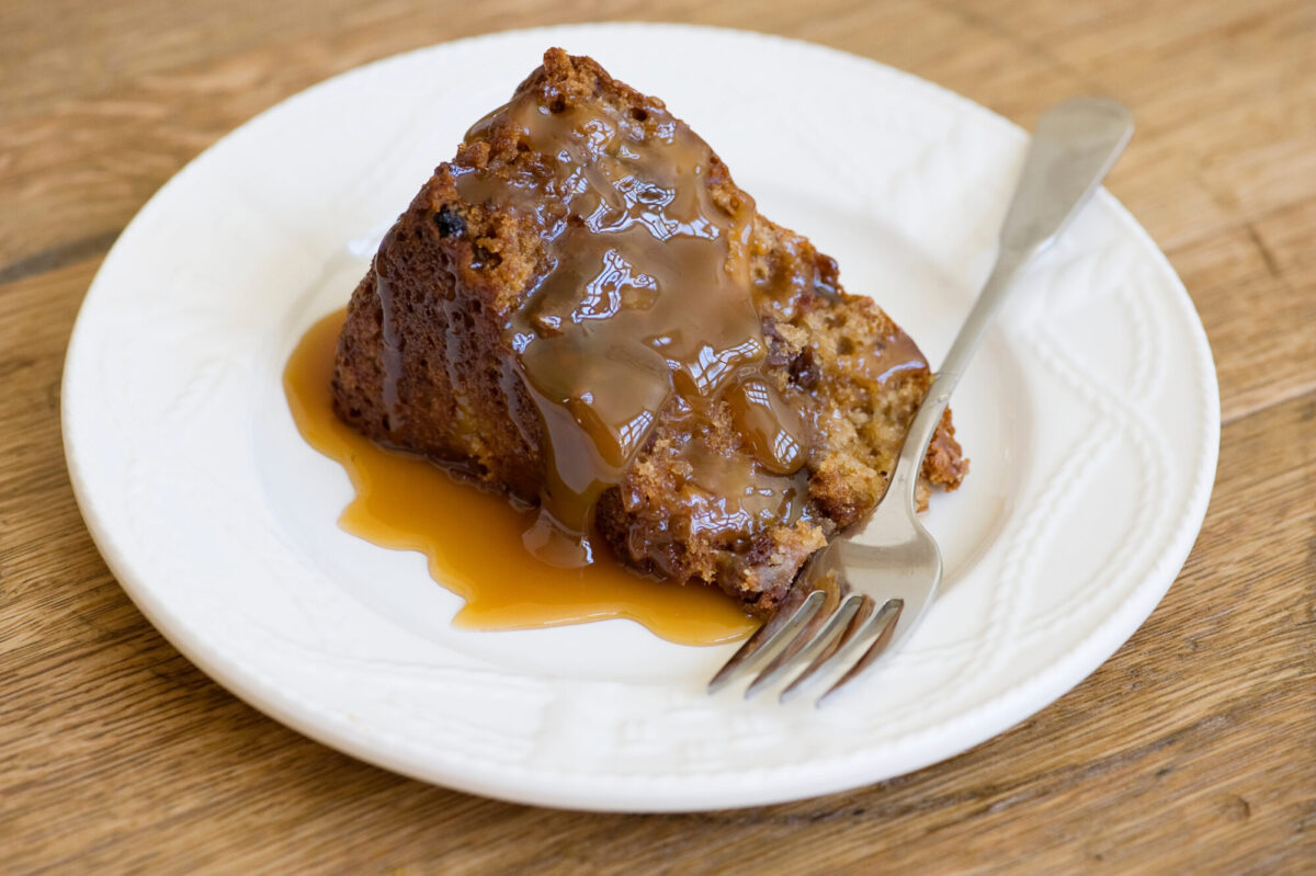 Slice of apple cake covered with caramel sauce on a plate with a fork.