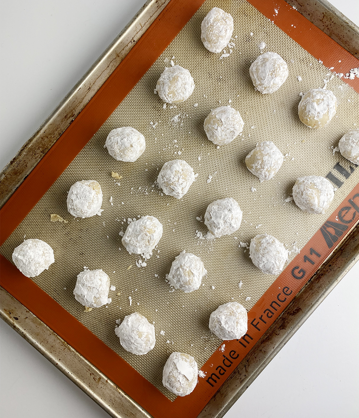 Finished rum balls covered in powdered sugar on a cookie sheet.