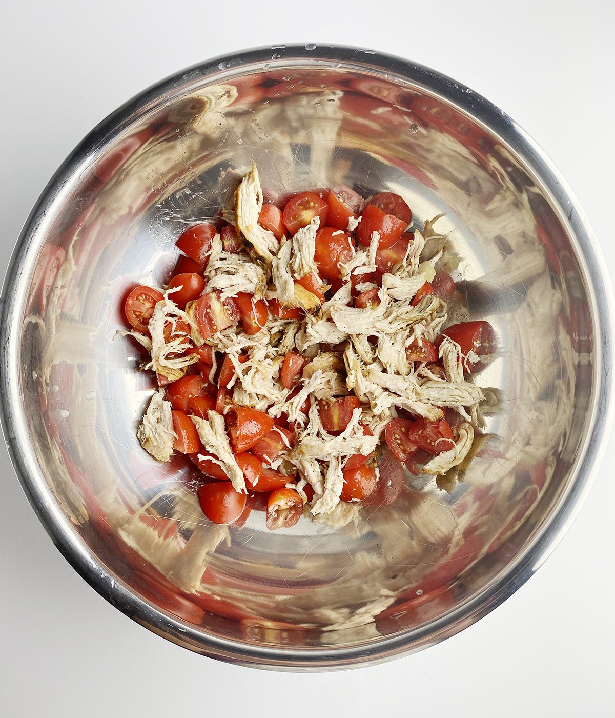 Chicken and tomatoes tossed in a bowl.