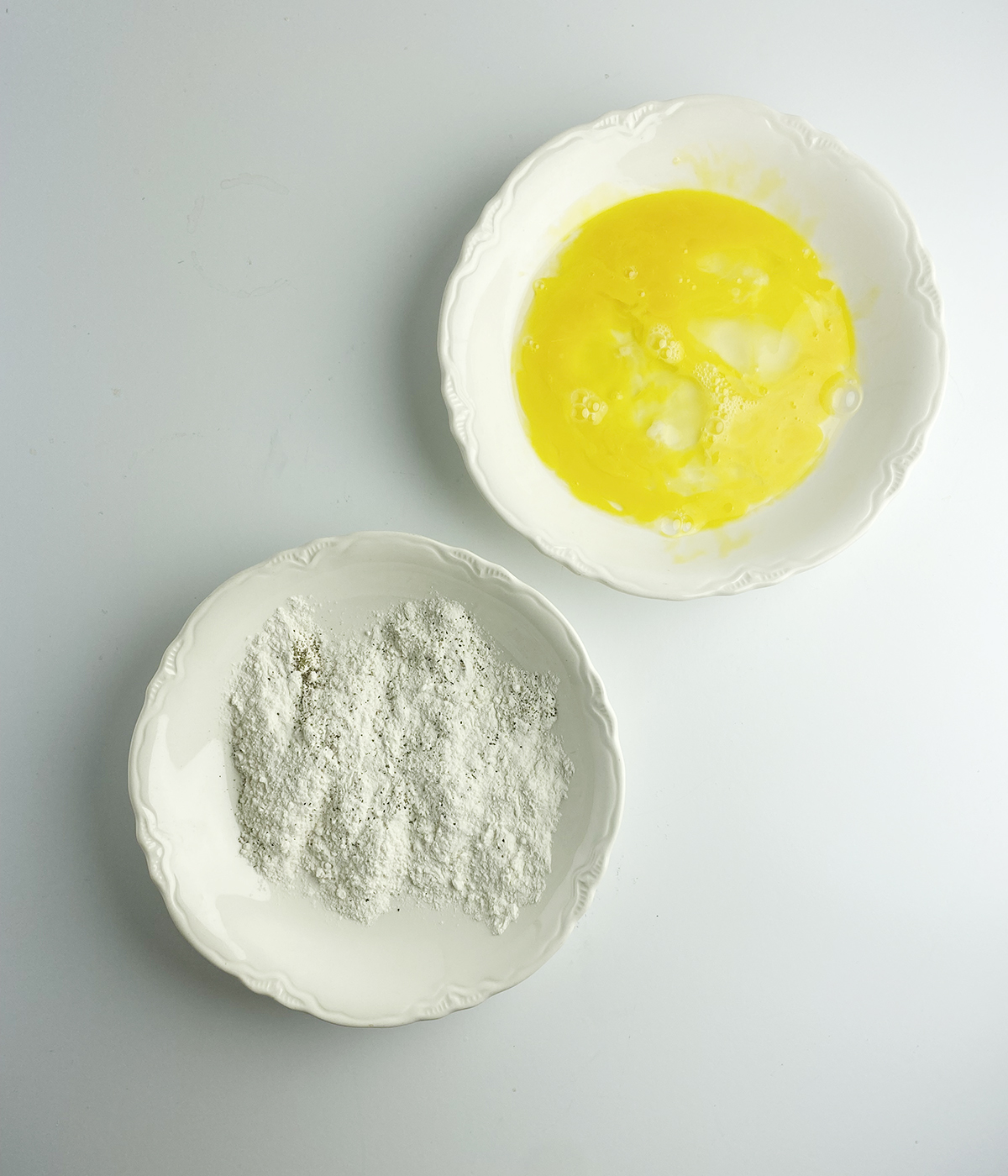 Eggs and flour in shallow bowls.