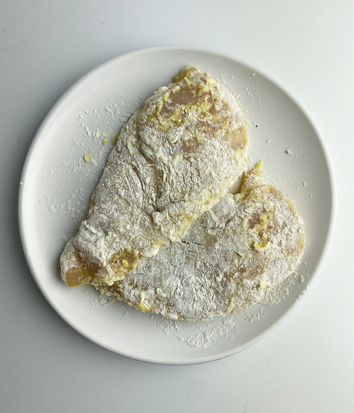 Floured chicken cutlets on a cutting board.