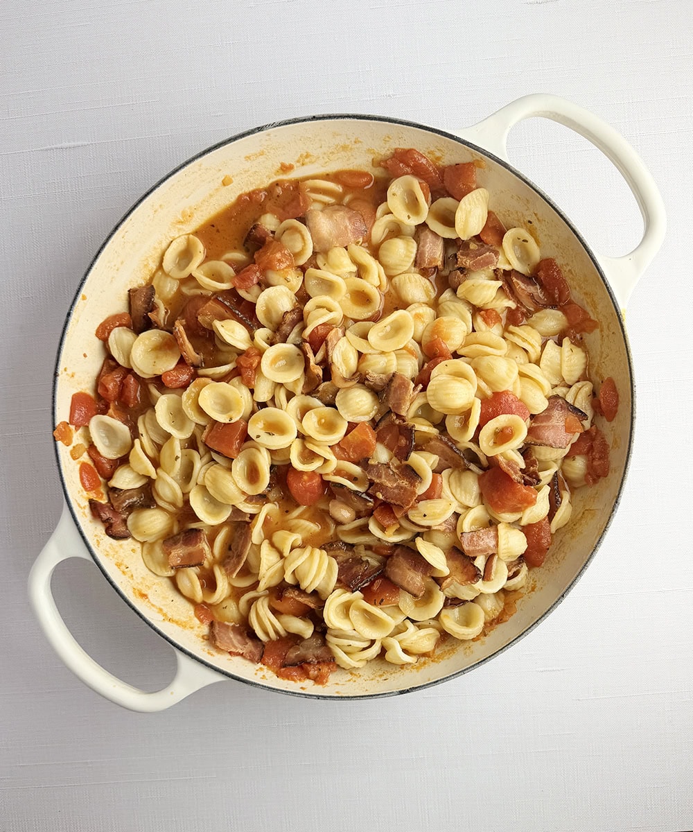 Pasta with tomato bacon sauce in a skillet.
