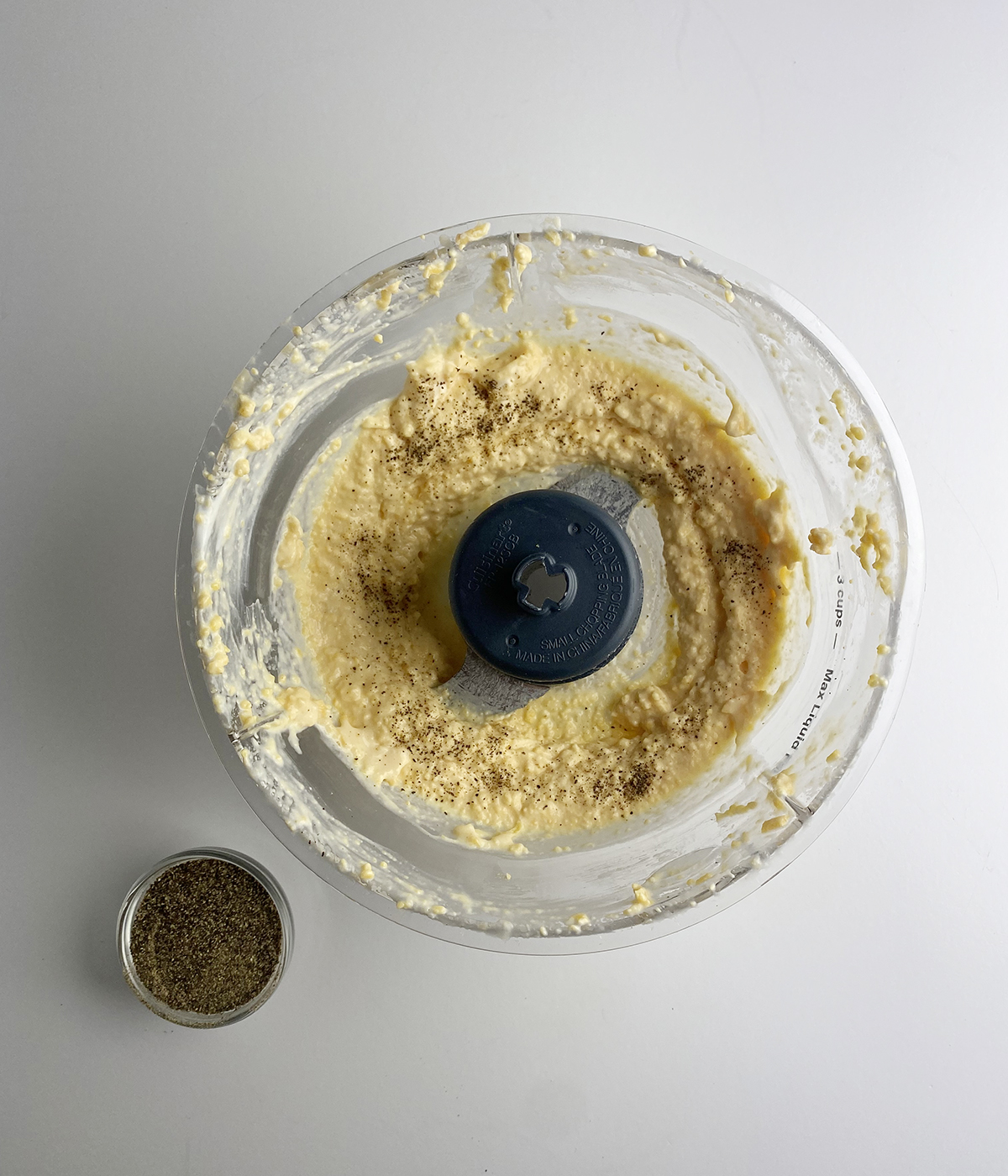 Cheese spread in a food processor with pepper on the side.