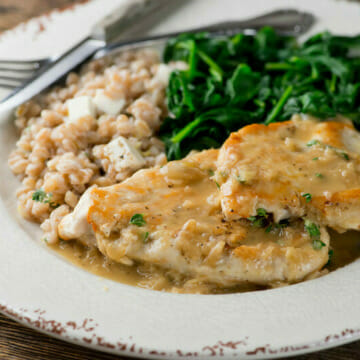 Plate of chicken in white wine pan sauce with spinach and barley on the side.