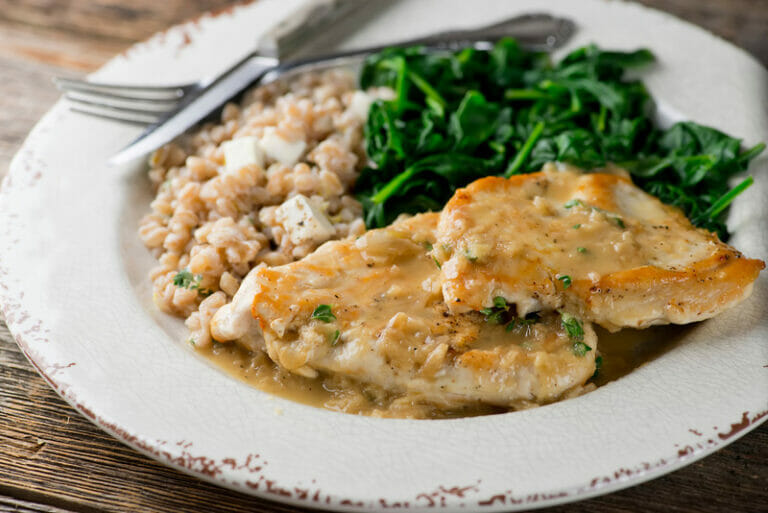 Plate of chicken in white wine pan sauce with spinach and barley on the side.
