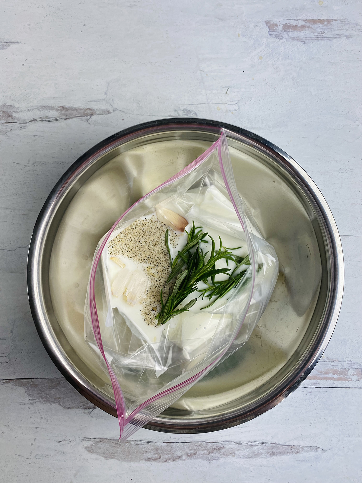 Buttermilk steak marinade ingredients in a plastic bag sitting in a metal bowl.