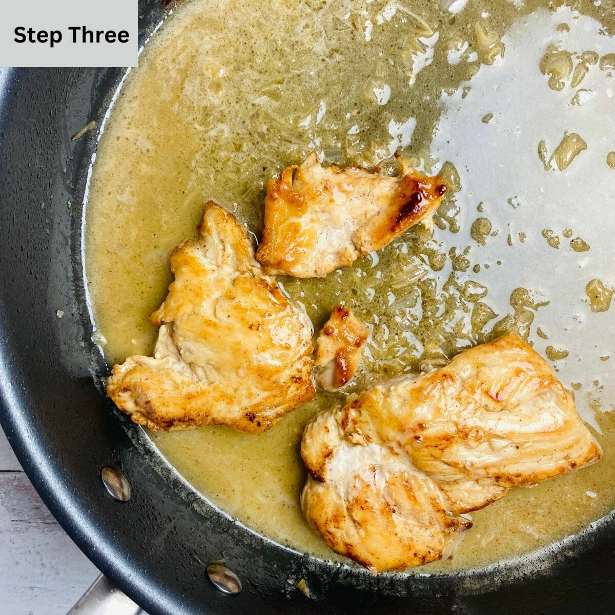 Chicken warming with buttered white wine sauce in a skillet.