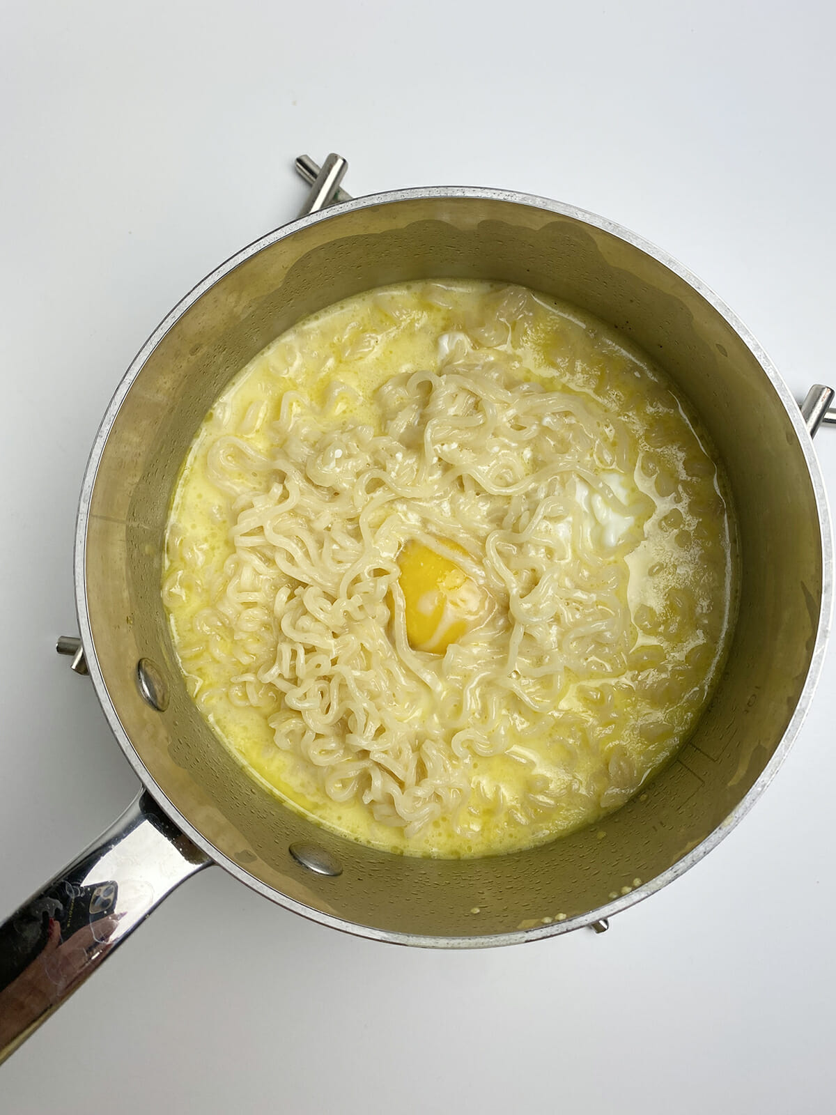 Egg poaching in a pot of cheesy ramen.