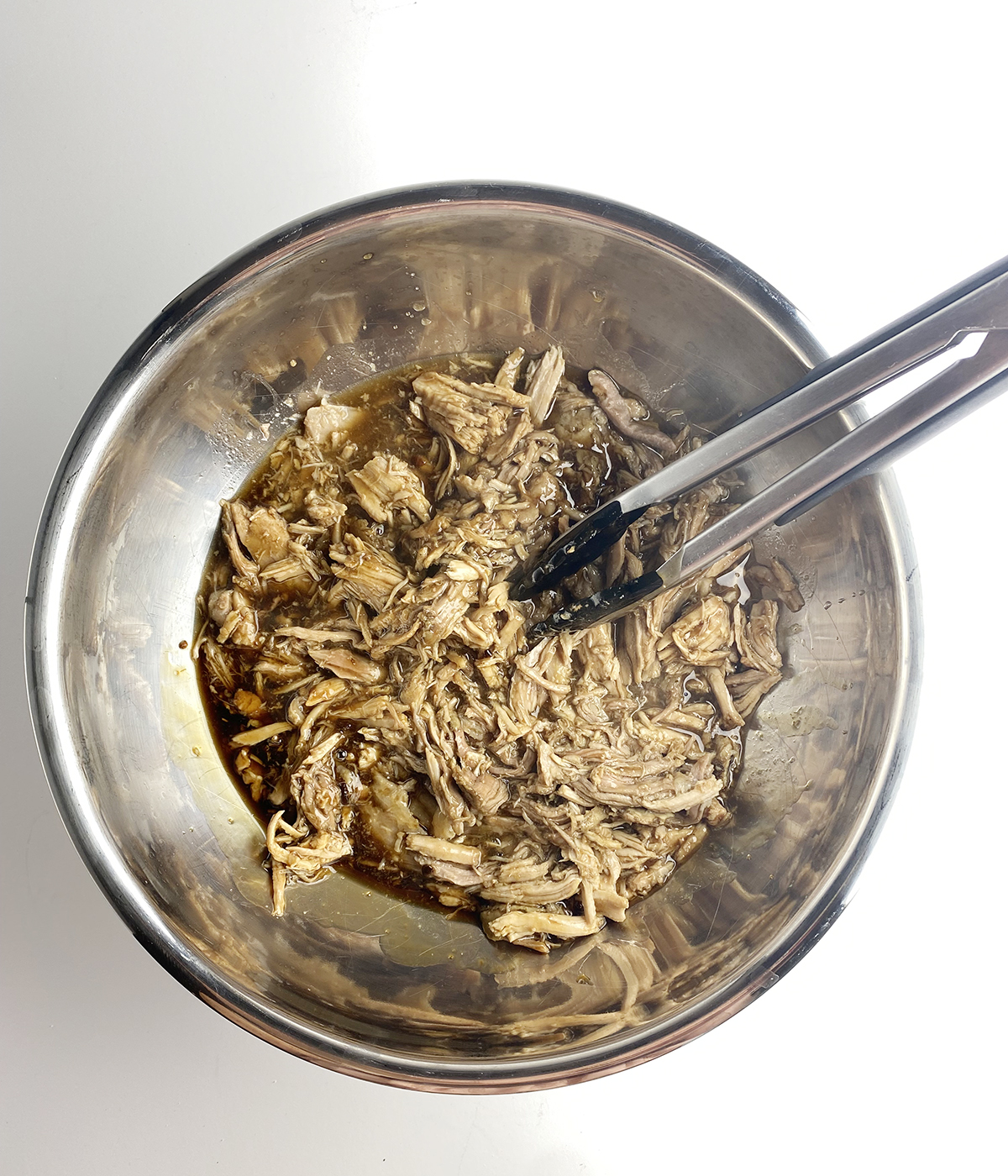 Shredded pork mixed with sauce in a metal bowl.