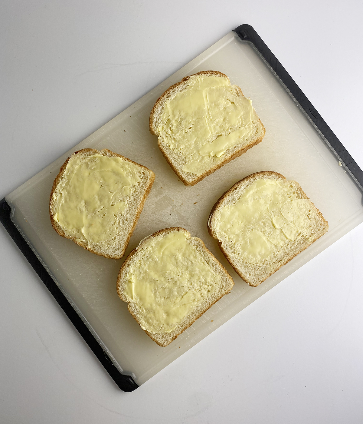 Four slices of buttered bread on a cutting board.