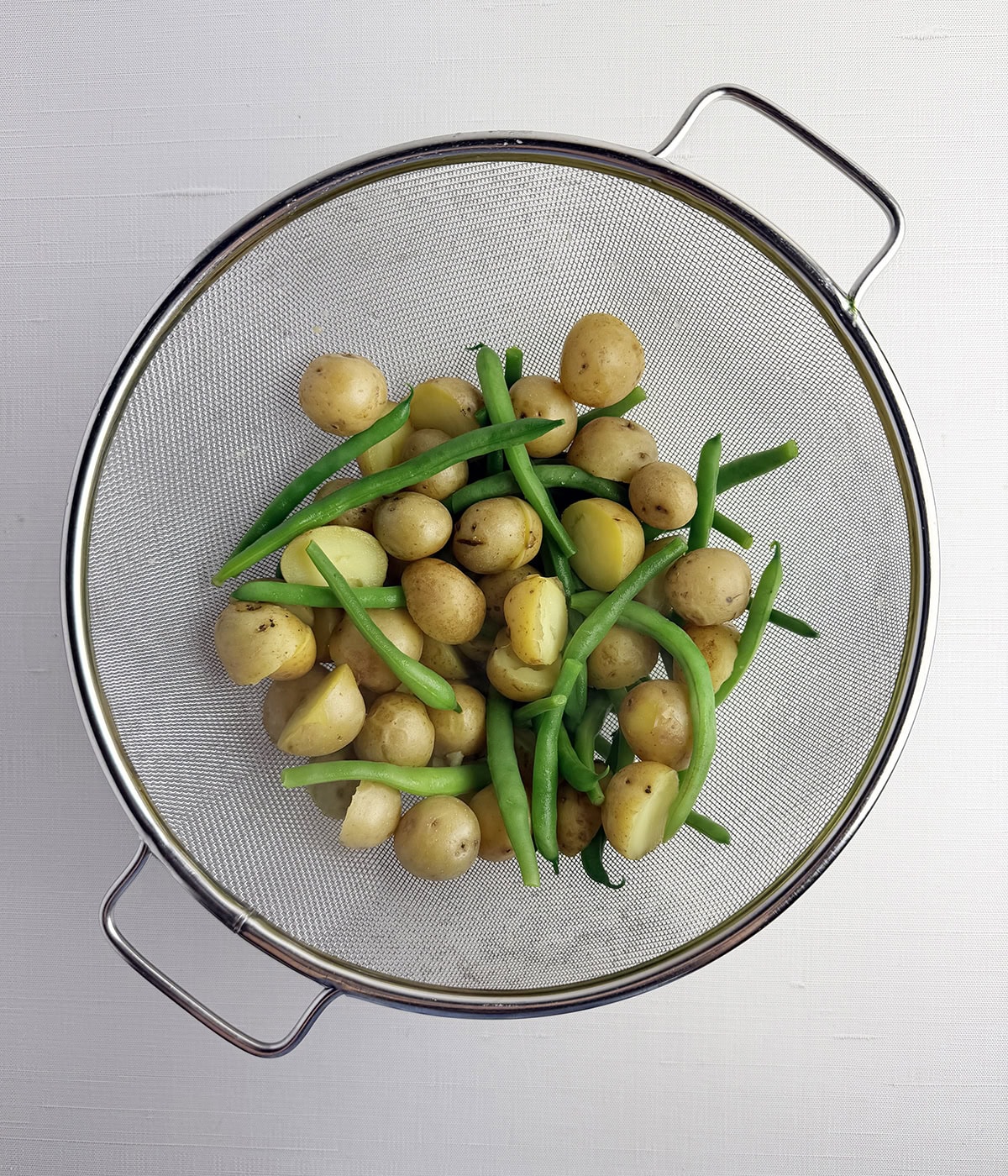 Cooked baby potatoes and green beans in a strainer.