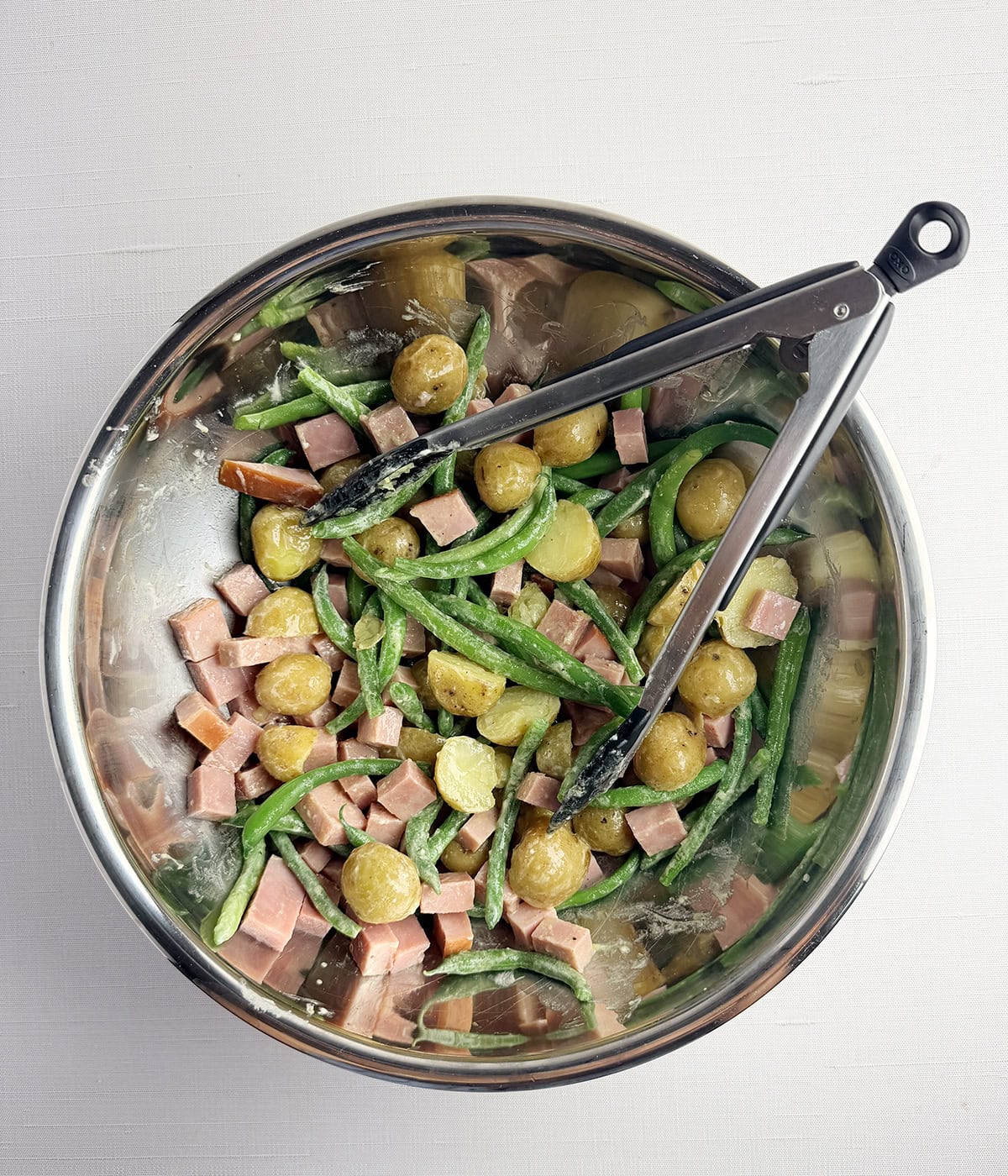 Ham and potato salad with dressing in a mixing bowl.