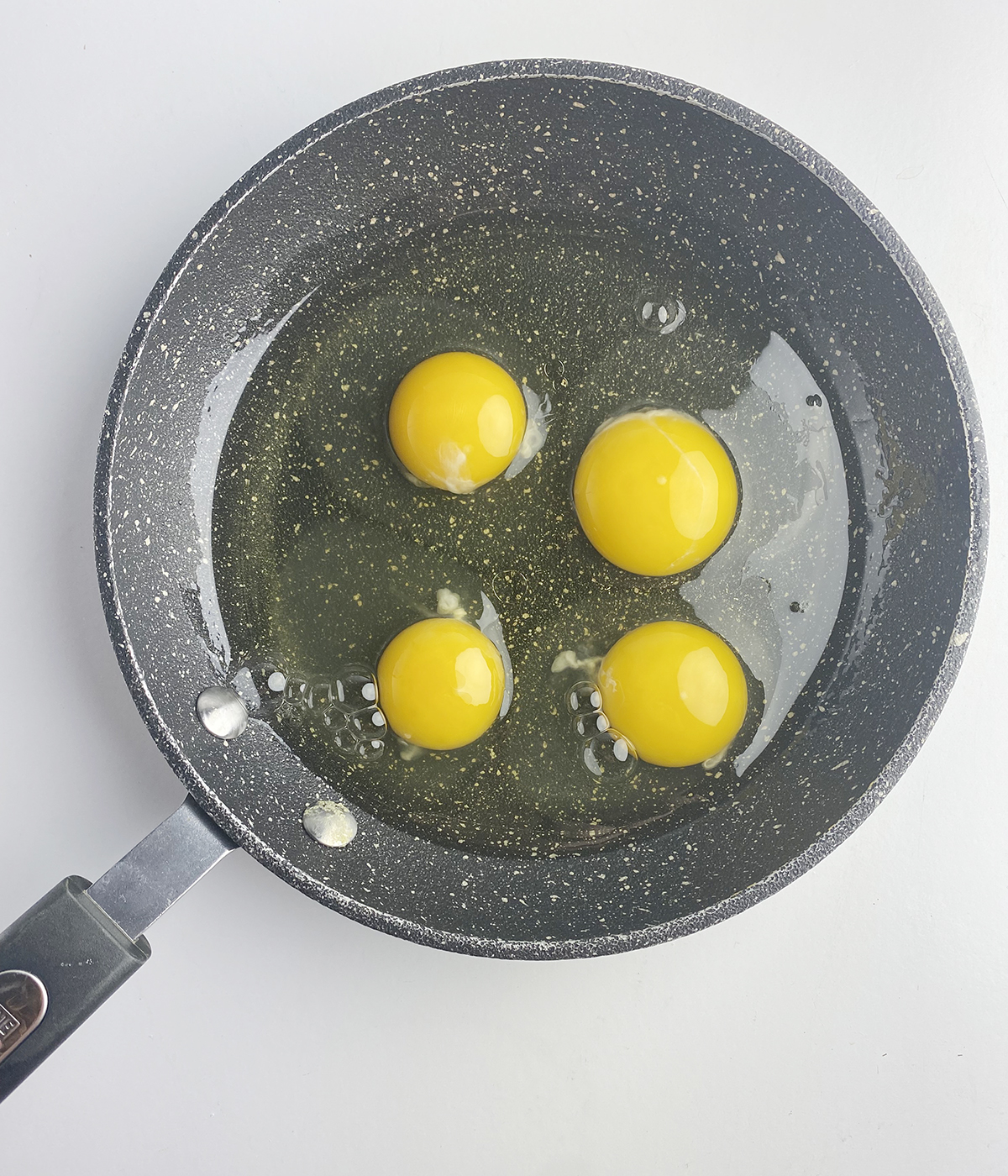 Four eggs in a cool skillet ready to be cooked.