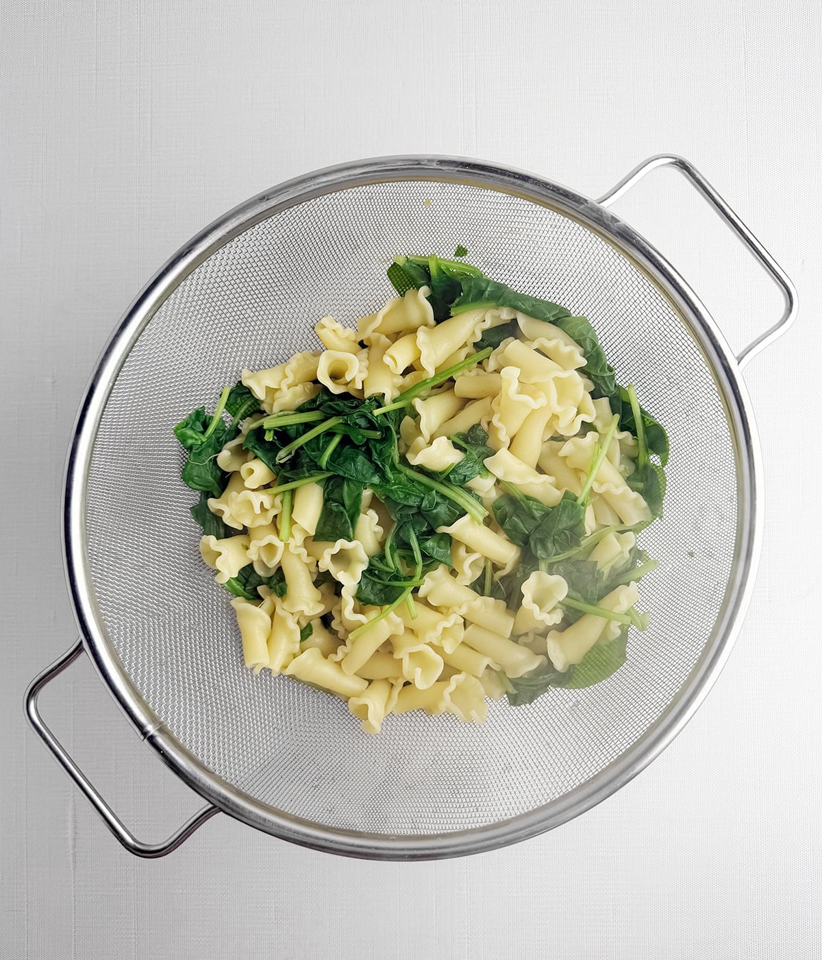 Pasta and spinach in a strainer.