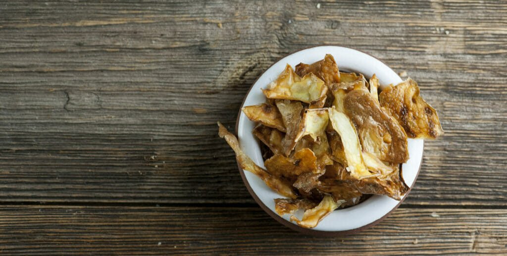 potato peelings chips Bowl of potato peel chips on a wooden counter.