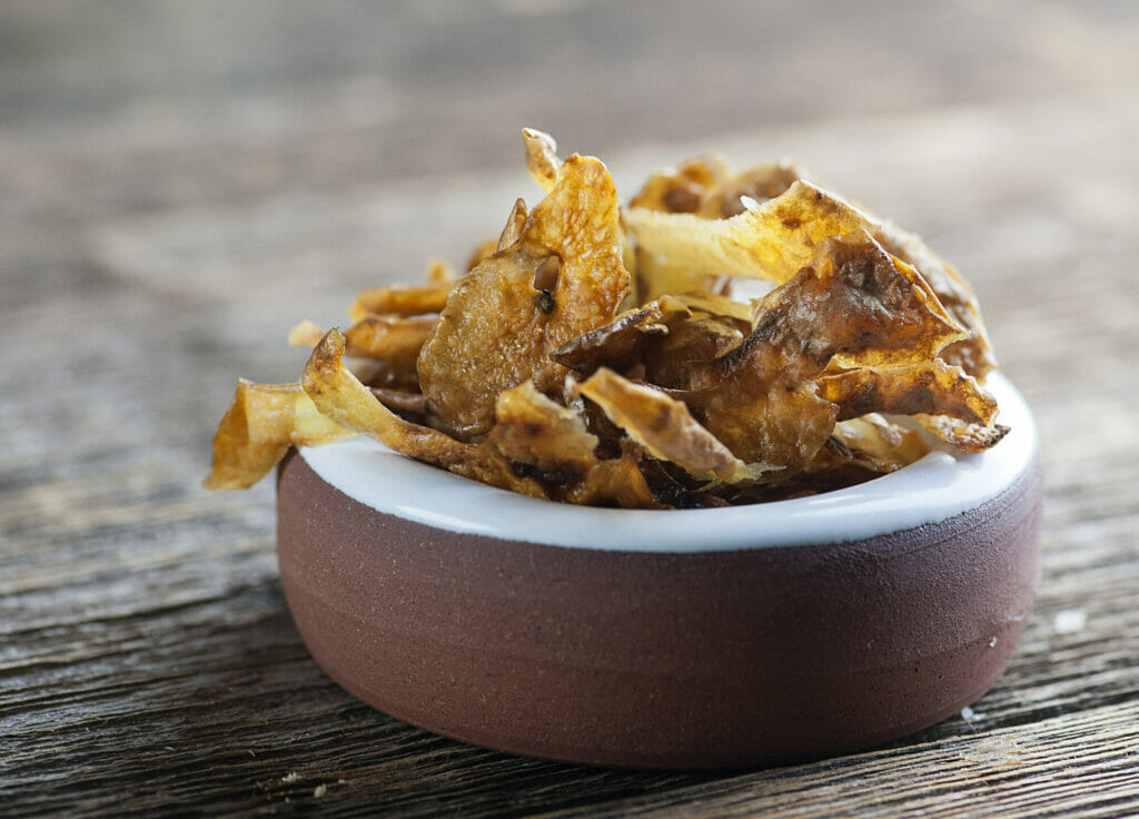 Small bowl of potato peel chips on a wooden counter.