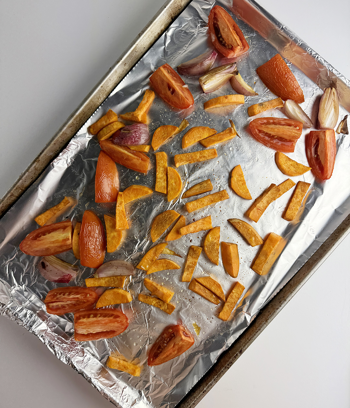 Roasted tomatoes and sweet potatoes on a baking pan.