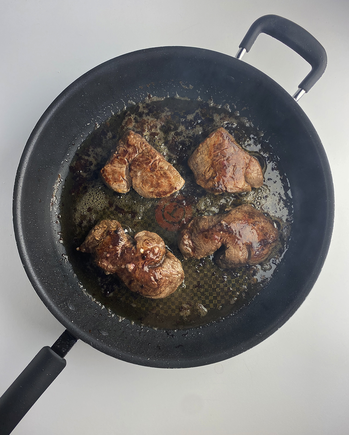 Steaks cooking in a pan.