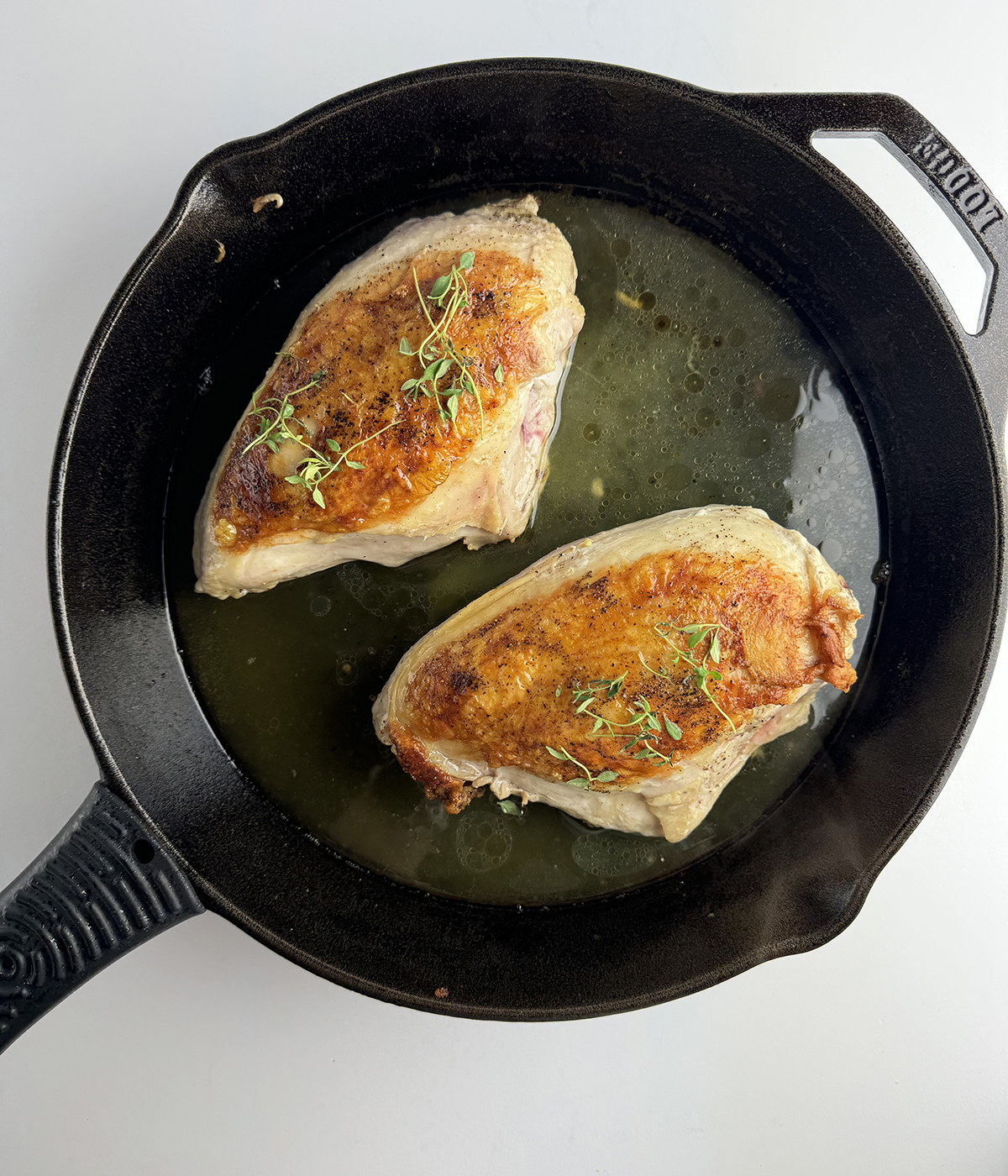 Chicken baking with fresh herbs in a skillet.